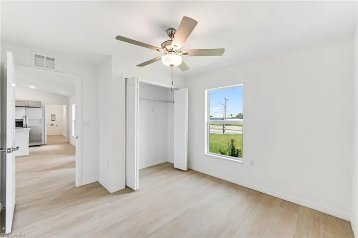 Unfurnished bedroom with light wood-style floors, a closet, visible vents, and stainless steel fridge with ice dispenser