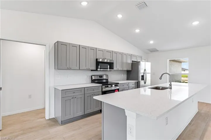 Kitchen featuring gray cabinetry, stainless steel appliances, a sink, visible vents, and light wood finished floors