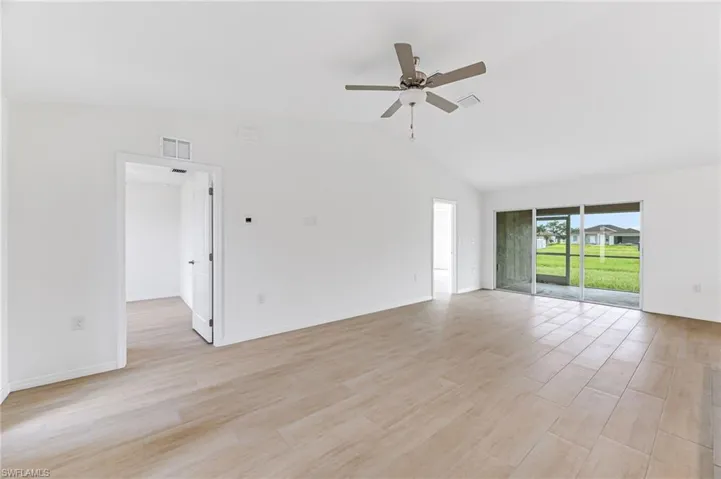 Spare room featuring light wood-type flooring, ceiling fan, visible vents, and vaulted ceiling