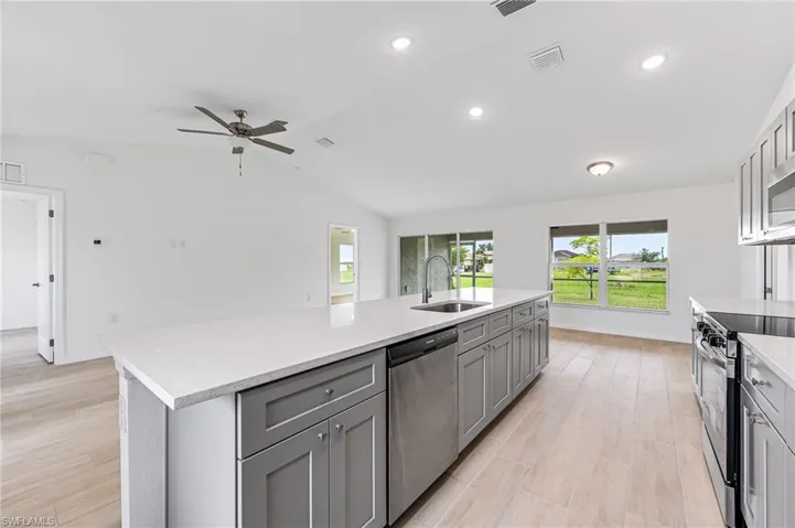 Kitchen featuring light countertops, gray cabinetry, appliances with stainless steel finishes, a kitchen island with sink, and a sink