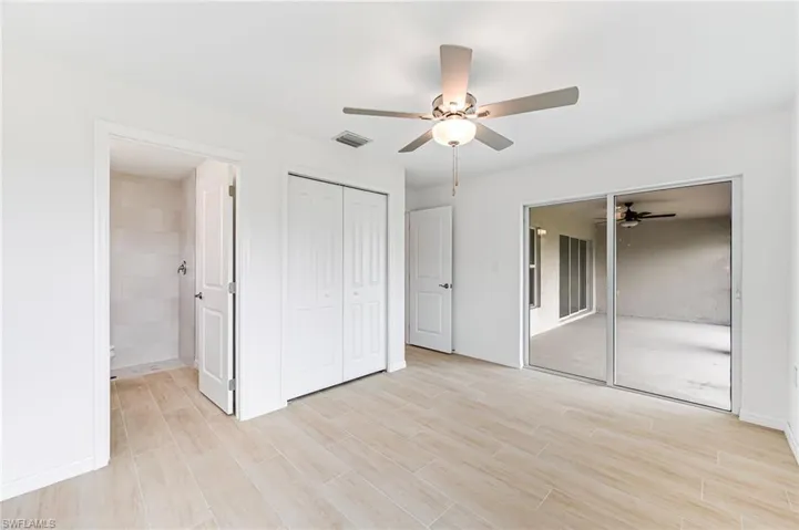 Unfurnished bedroom with visible vents, light wood-style floors, ceiling fan, ensuite bath, and baseboards