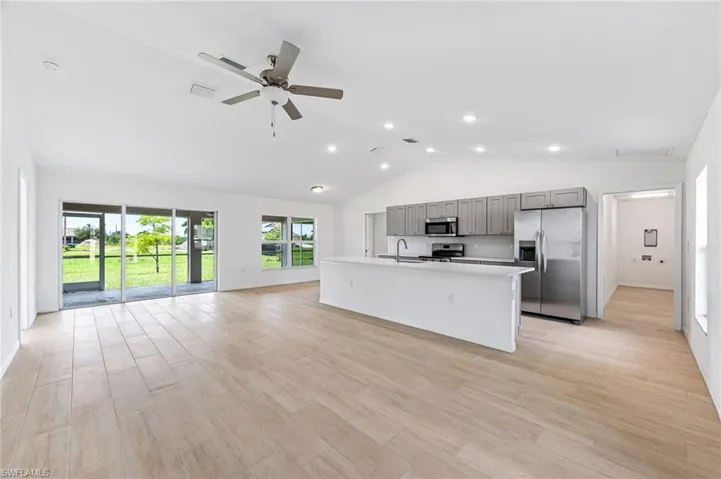 Kitchen with light countertops, gray cabinetry, applianceswith stainless steel finishes, open floor plan, and an island with sink. Picture is of finished model