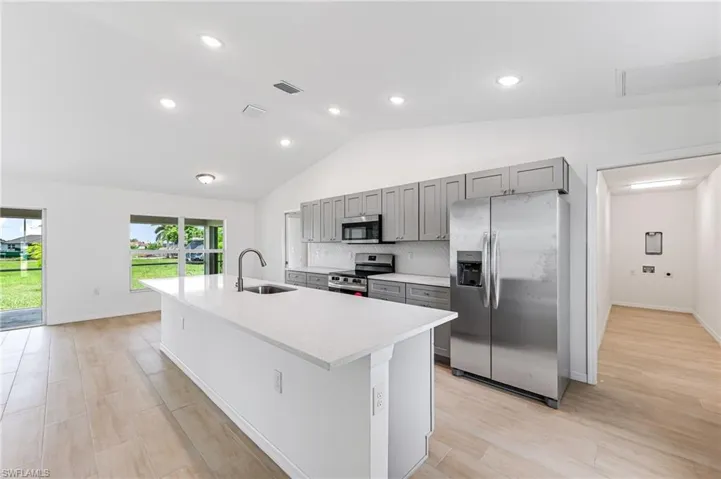 Kitchen featuring light countertops, gray cabinetry, appliances with stainless steel finishes, a sink, and an island with sink
