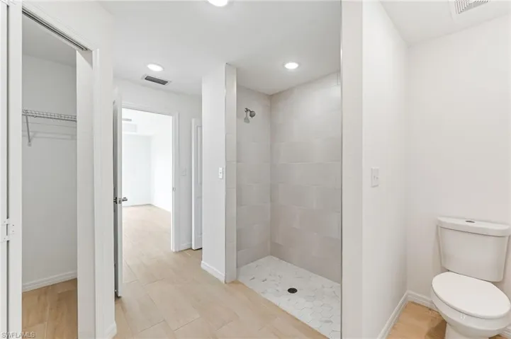 Bathroom featuring toilet, wood finished floors, visible vents, baseboards, and tiled shower