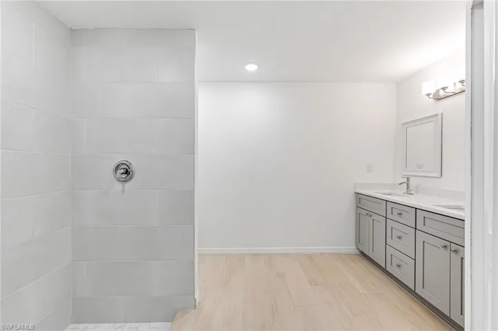 Full bath featuring double vanity, baseboards, wood finished floors, a tile shower, and a sink