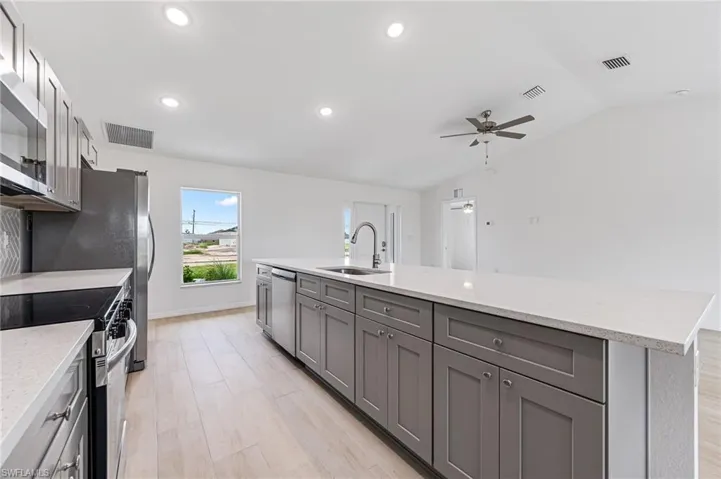 Kitchen featuring stainless steel appliances, visible vents, gray cabinetry, vaulted ceiling, and a sink