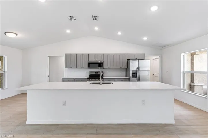 Kitchen with stainless steel appliances, a sink, a large island with sink, and gray cabinetry