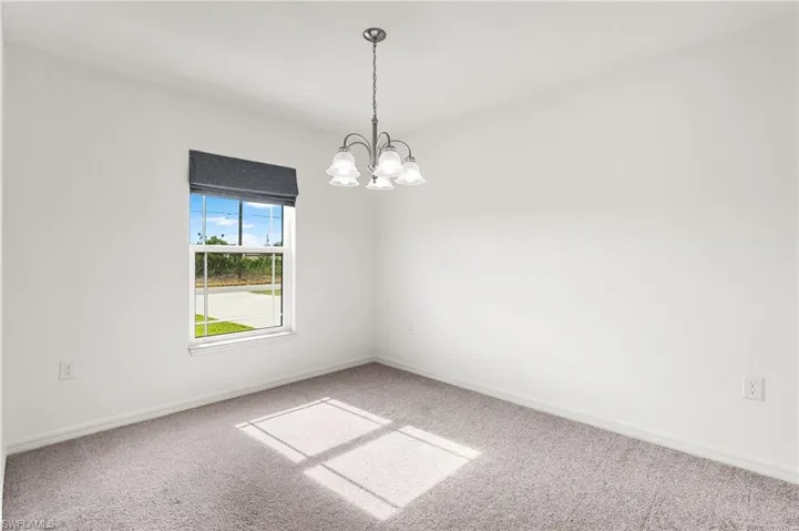 Empty room with carpet floors and an inviting chandelier