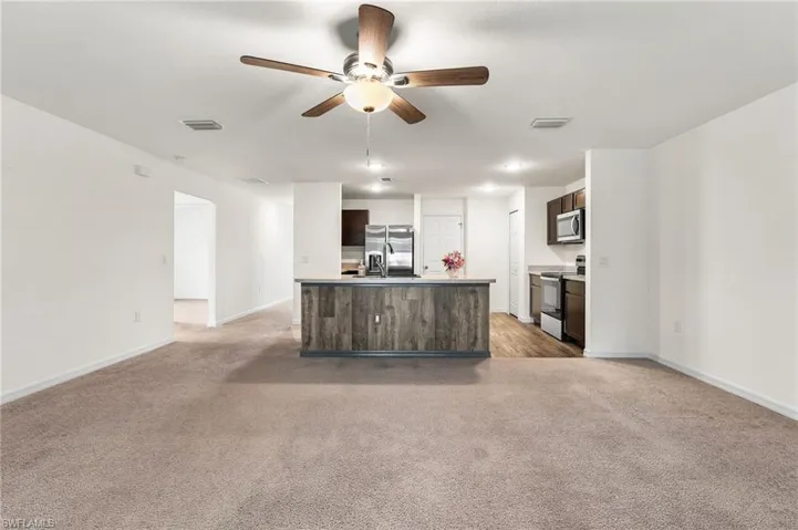 Kitchen with a kitchen island with sink, light carpet, sink, dark brown cabinetry, and stainless steel appliances