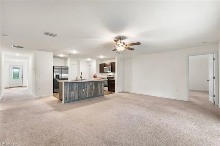 Kitchen featuring light colored carpet, dark brown cabinetry, a kitchen island with sink, and appliances with stainless steel finishes