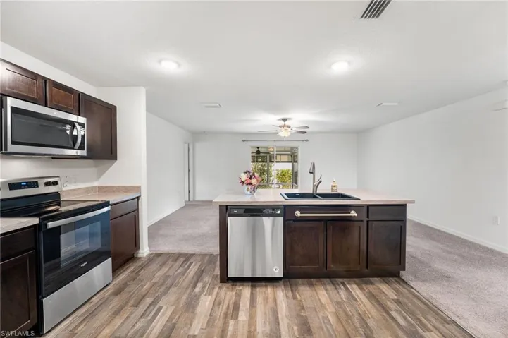 Kitchen featuring dark colored carpet, appliances with stainless steel finishes, dark brown cabinetry, and sink