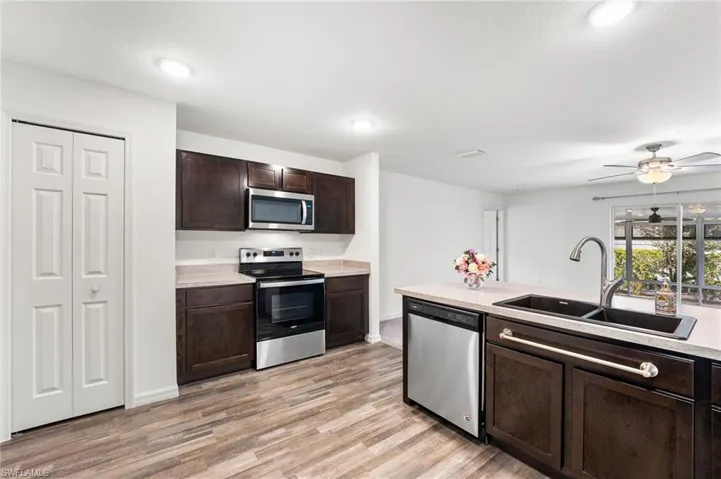 Kitchen featuring light wood-type flooring, dark brown cabinets, stainless steel appliances, ceiling fan, and sink