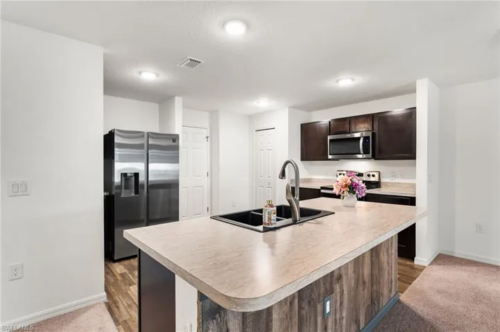 Kitchen with carpet flooring, sink, stainless steel appliances, a center island with sink, and dark brown cabinets