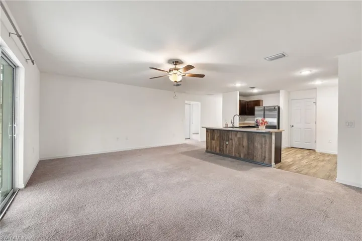 Unfurnished living room featuring ceiling fan and light carpet