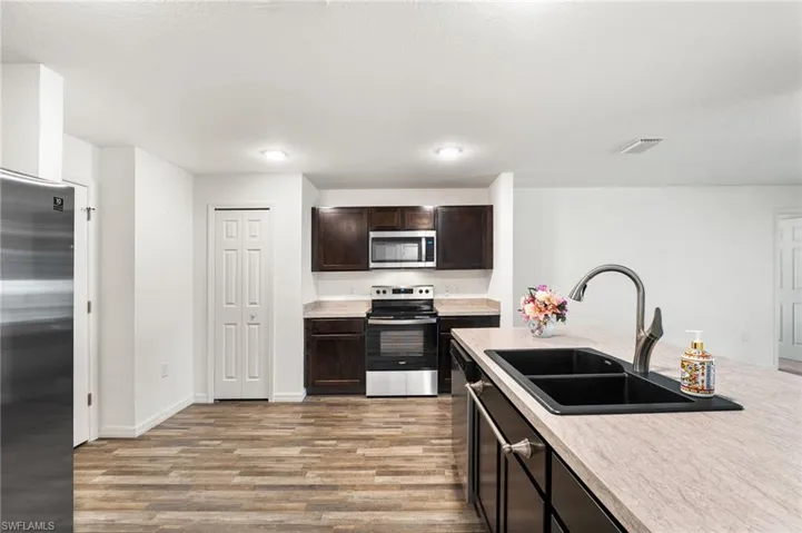 Kitchen with dark brown cabinetry, sink, stainless steel appliances, and light hardwood / wood-style flooring