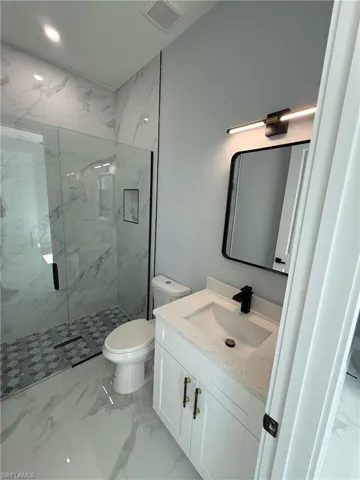 Bathroom featuring light marble finish flooring, a marble finish shower, and vanity