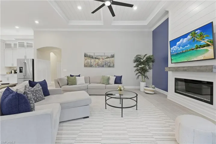 Living area with arched walkways, a glass covered fireplace, recessed lighting, light wood finished floors, and crown molding