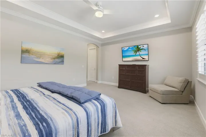 Carpeted bedroom featuring arched walkways, a raised ceiling, crown molding, recessed lighting, and a ceiling fan