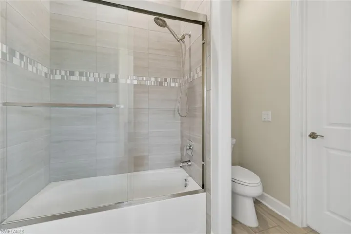 Full bath featuring combined bath / shower with glass door and toilet