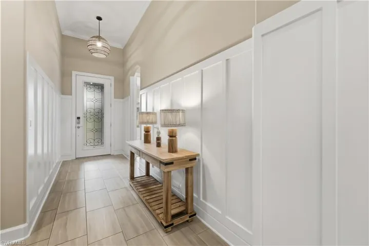 Doorway featuring a decorative wall, crown molding, a wainscoted wall, and tile patterned floors