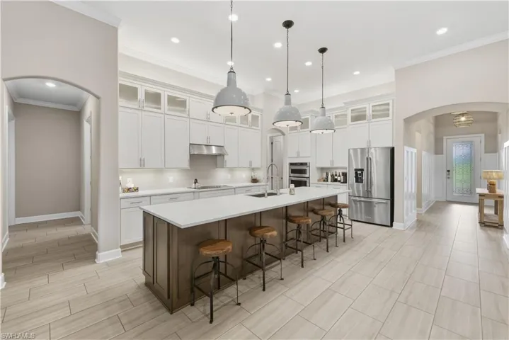 Kitchen featuring arched walkways, stainless steel appliances, a breakfast bar area, decorative backsplash, and white cabinets