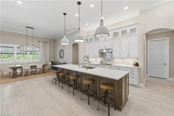 Kitchen featuring a kitchen bar, white cabinets, pendant lighting, decorative backsplash, and crown molding
