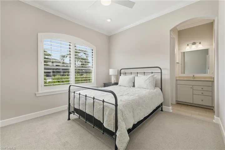 Bedroom with ornamental molding, ceiling fan, connected bathroom, and light colored carpet
