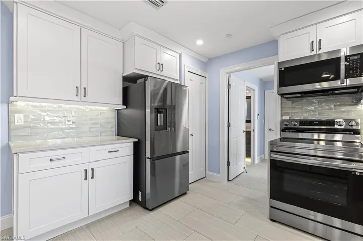 Kitchen featuring stainless steel appliances, tasteful backsplash, white cabinetry, light stone counters, and recessed lighting