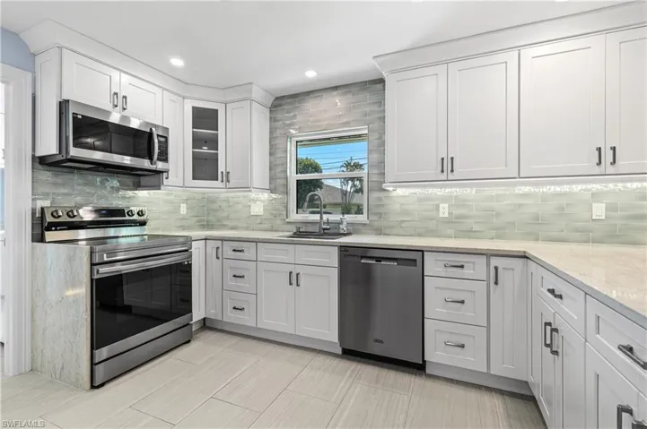 Kitchen featuring appliances with stainless steel finishes, backsplash, white cabinets, light stone counters, and recessed lighting