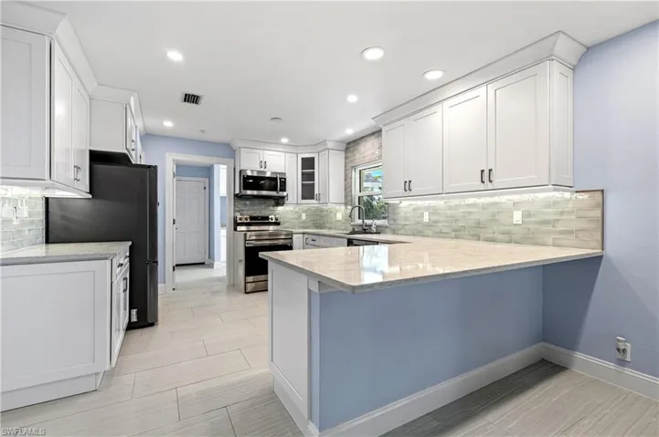Kitchen featuring stainless steel appliances, a peninsula, decorative backsplash, white cabinetry, and light stone countertops