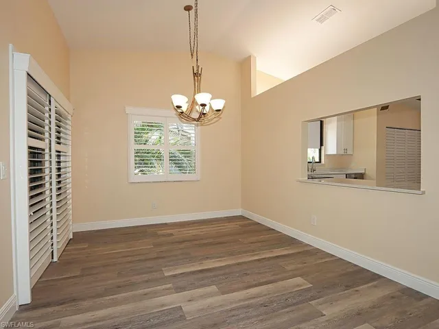 Unfurnished dining area with dark wood-style flooring, a chandelier, and lofted ceiling