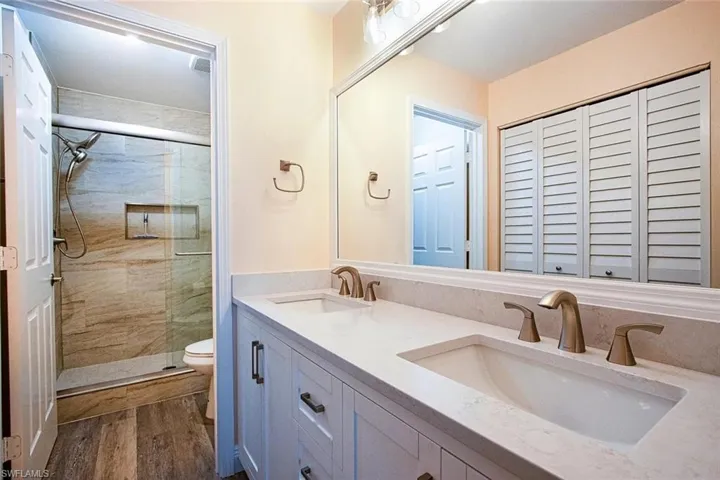 Bathroom featuring double vanity, a stall shower, dark wood-type flooring, and a closet