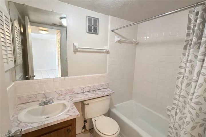 Bathroom featuring shower / bath combo, vanity, a textured ceiling, decorative backsplash, and tile walls