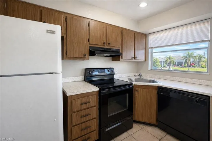 Kitchen featuring black appliances, light countertops, under cabinet range hood, light tile patterned floors, and brown cabinetry