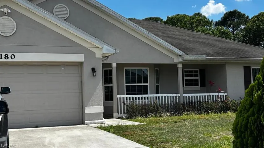 Stucco exterior featuring a covered front porch with white railing, contrasting dark shutters, and an attached two-car garage