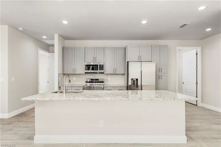 Kitchen featuring appliances with stainless steel finishes, sink, an island with sink, light wood-type flooring, and light stone counters