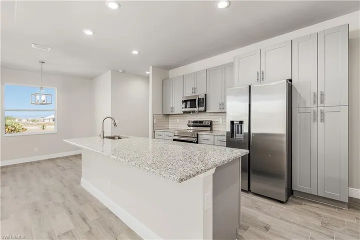 Kitchen with light hardwood / wood-style floors, stainless steel appliances, light stone countertops, and a center island with sink