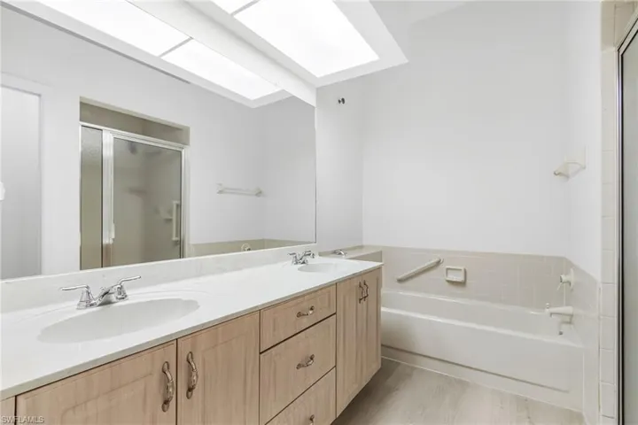 Full bath featuring a stall shower, double vanity, a garden tub, a skylight, and light wood finished floors