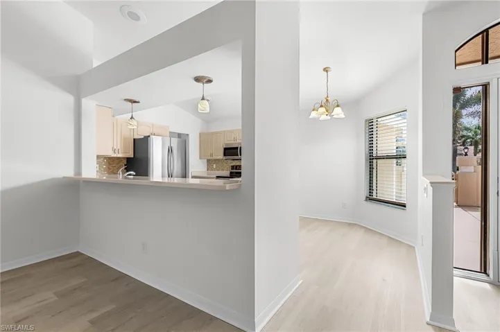 Kitchen with decorative backsplash, light wood finished floors, decorative light fixtures, vaulted ceiling, and stainless steel appliances