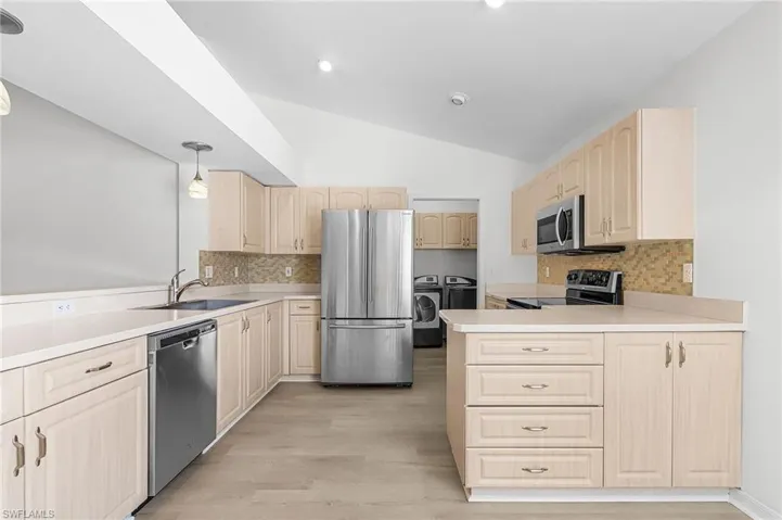Kitchen featuring stainless steel appliances, decorative backsplash, a peninsula, independent washer and dryer, and light countertops