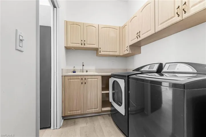 Laundry room with washer and clothes dryer, light wood finished floors, and cabinet space