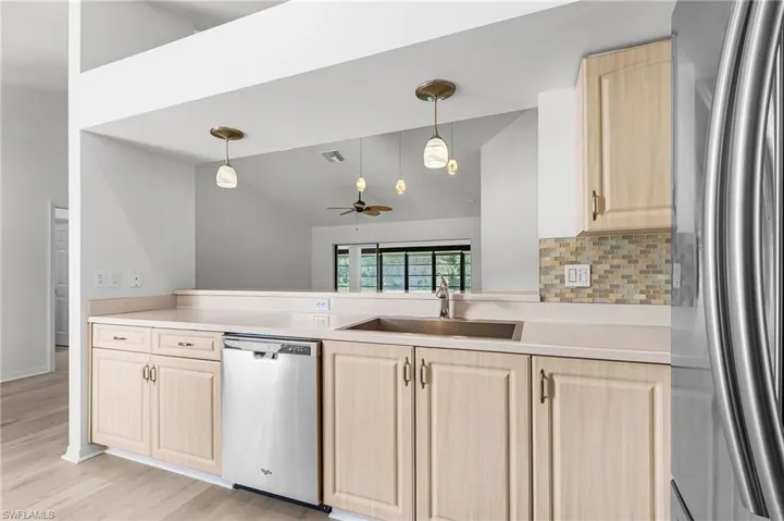 Kitchen featuring light brown cabinetry, appliances with stainless steel finishes, light countertops, backsplash, and lofted ceiling