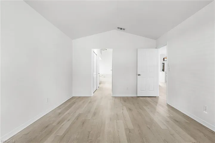 Unfurnished bedroom with light wood-type flooring, vaulted ceiling, and ensuite bath