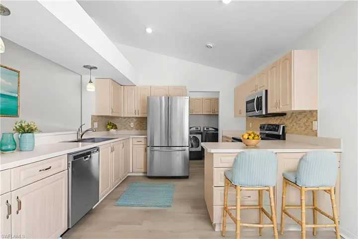 Kitchen with tasteful backsplash, stainless steel appliances, light countertops, and vaulted ceiling