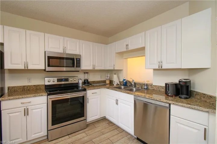 Kitchen with sink, a textured ceiling, light hardwood / wood-style flooring, white cabinetry, and stainless steel appliances