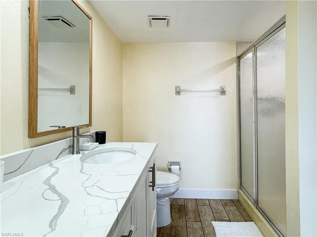 Bathroom with vanity, toilet, an enclosed shower, and hardwood / wood-style flooring