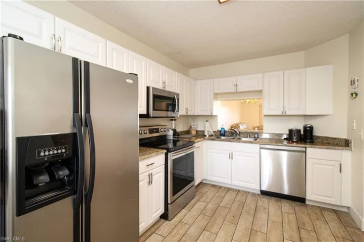 Kitchen with light wood-type flooring, a textured ceiling, sink, white cabinets, and stainless steel appliances