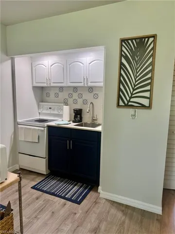 Kitchen with white electric range, light wood-style floors, white cabinets, and backsplash