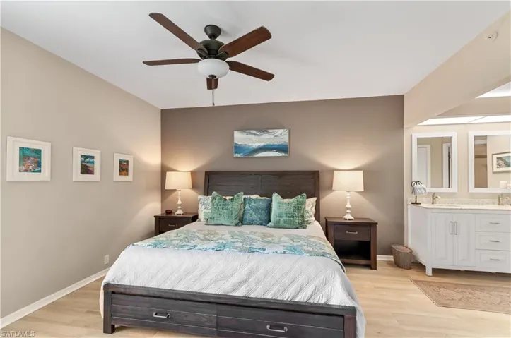 Bedroom with light wood-style floors, ceiling fan, ensuite bath, and baseboards
