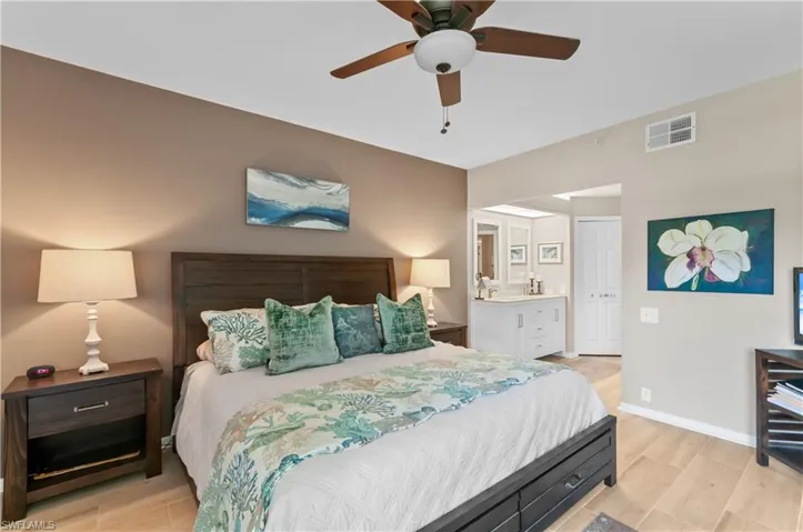 Bedroom with ensuite bathroom, ceiling fan, wood finish floors, visible vents, and baseboards